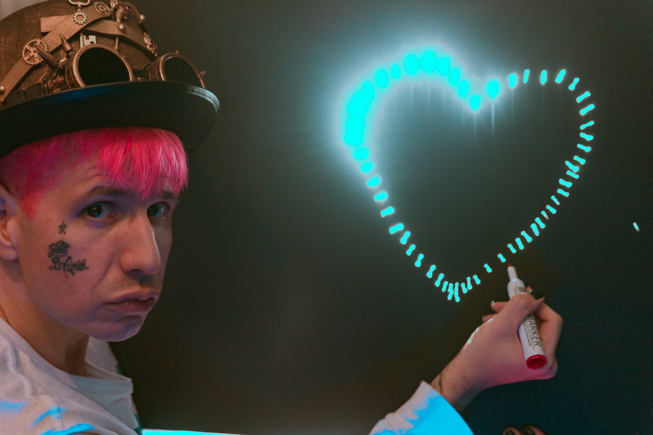 Editorial press photo of Lord Infinit3 with hot pink hair drawing a glowing cyan heart